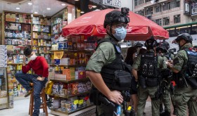 A pharmacy sales person sits on a chair as riot police officers stop and search people on the vicinity during a banned protest in Hong Kong, China, on October 1, 2020.